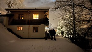 Una casa de dos pisos con un balcón, rodeada de árboles cubiertos de nieve.