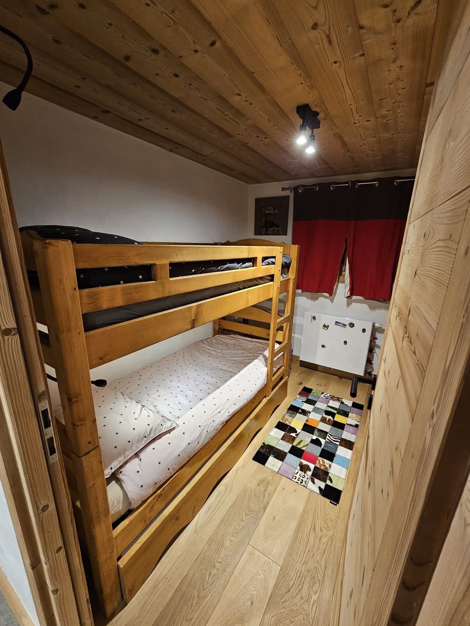 A bunk bed room with a wooden ceiling, a white dresser, and a colorful quilt on the floor.