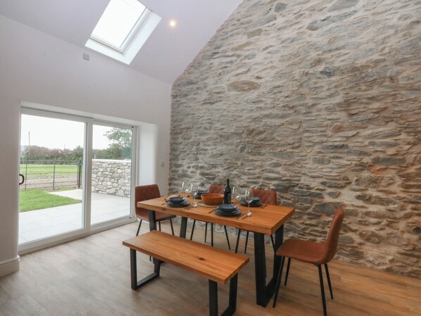 A dining area with a stone wall, a wooden table, and benches. - Beudy Tanrallt (Holyhead)