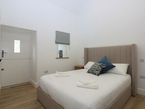 Une chambre à coucher comprenant un lit, une table de chevet, une commode, une fenêtre avec un store et une porte.