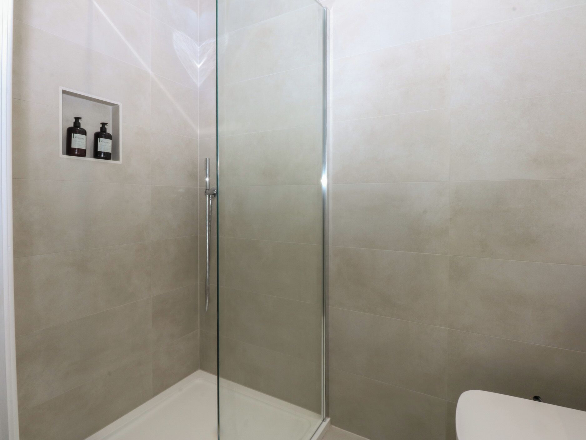 A glass-enclosed shower with beige tiles and a white toilet visible to the right.