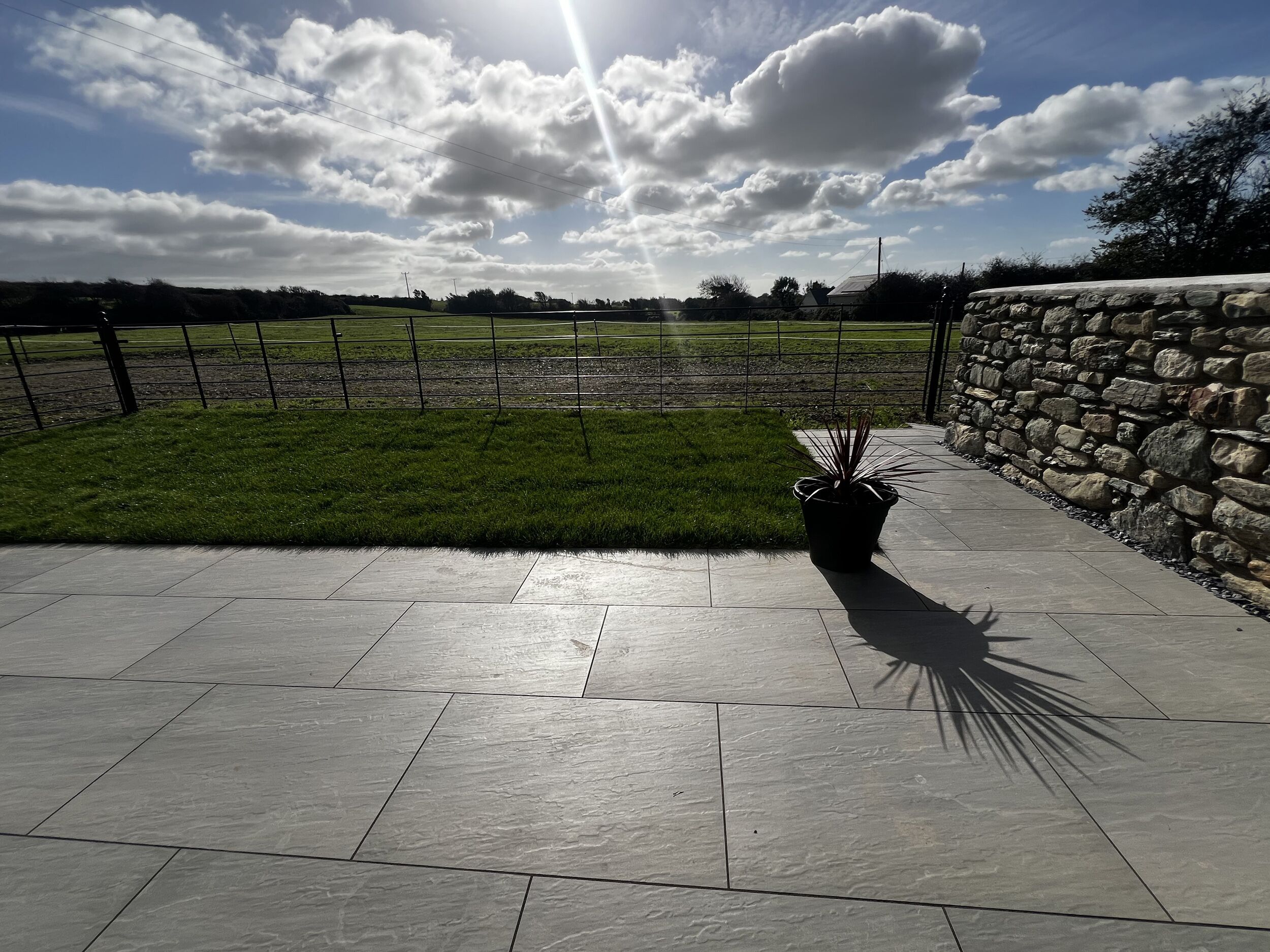 A paved patio with a stone wall and a grassy area.