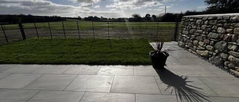 A paved patio with a stone wall and a grassy area.