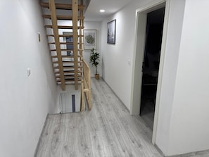 Un couloir avec un escalier en bois, une plante en pot et une œuvre d’art encadrée accrochée au mur.
