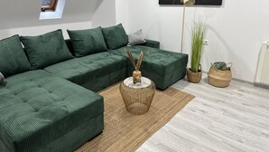 A modern living room with a sectional sofa, a floor lamp, a painting, and a potted plant.