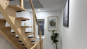 A wooden staircase leading to a landing with a framed leaf artwork and a potted plant.