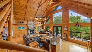 A spacious cabin with a stone fireplace, wooden floors, and large windows offering scenic views.
