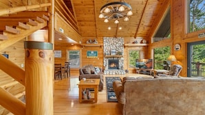 A cozy cabin interior with a stone fireplace, wooden walls, and a large window overlooking greenery.
