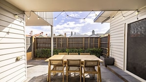A covered patio with a wooden table and chairs, a view of the neighborhood, and a fence. - Modern 3BR Executive Townhouse in CBD, Mibnb (Geelong)