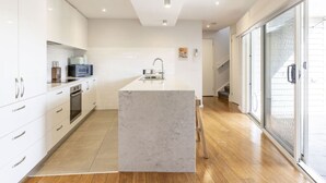 A modern kitchen with white cabinetry, a marble island, and a sliding glass door leading to a balcony. - Modern 3BR Executive Townhouse in CBD, Mibnb (Geelong)