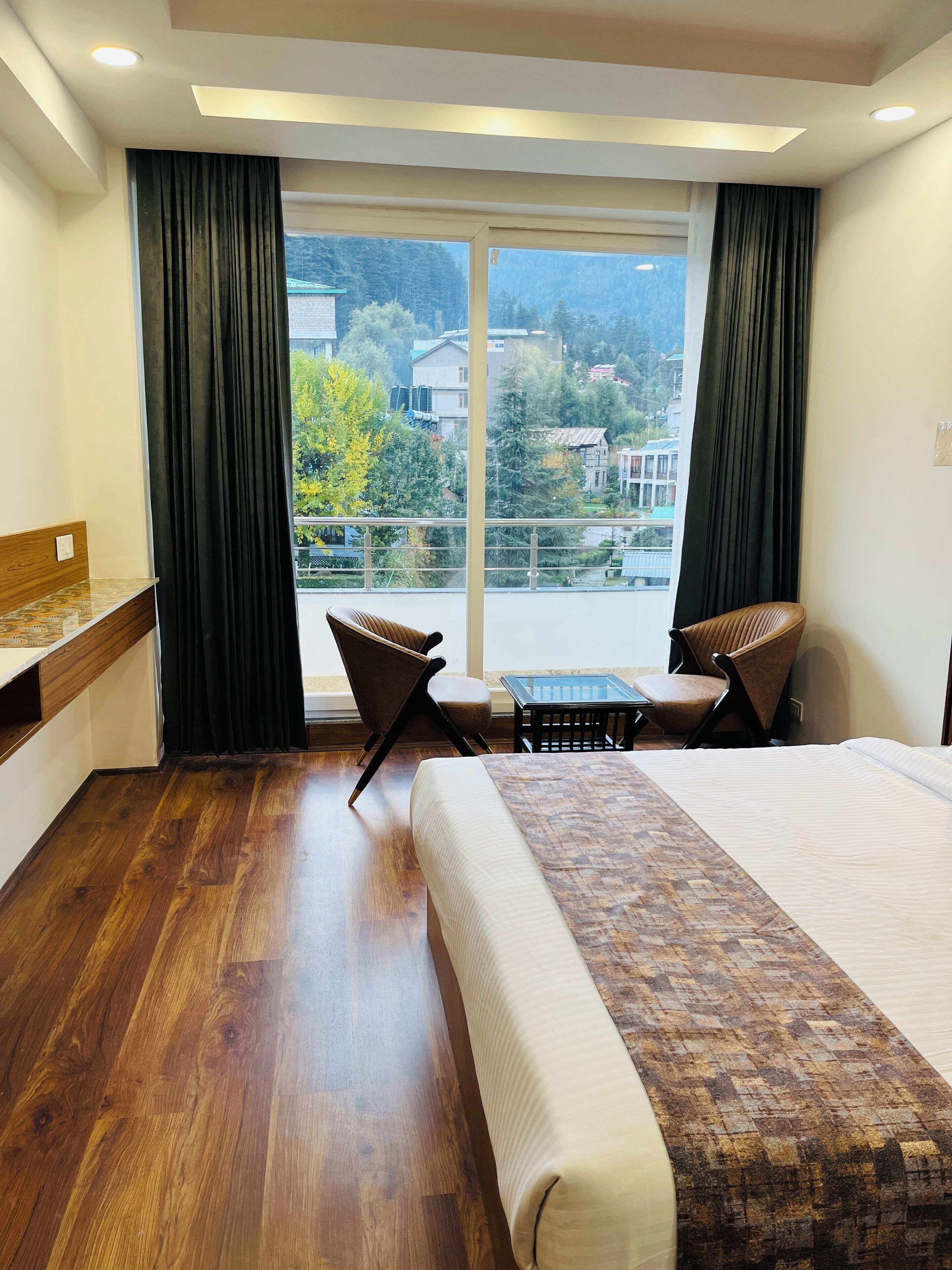 A hotel room with a large bed, two chairs, a small table, and a view of the outside.