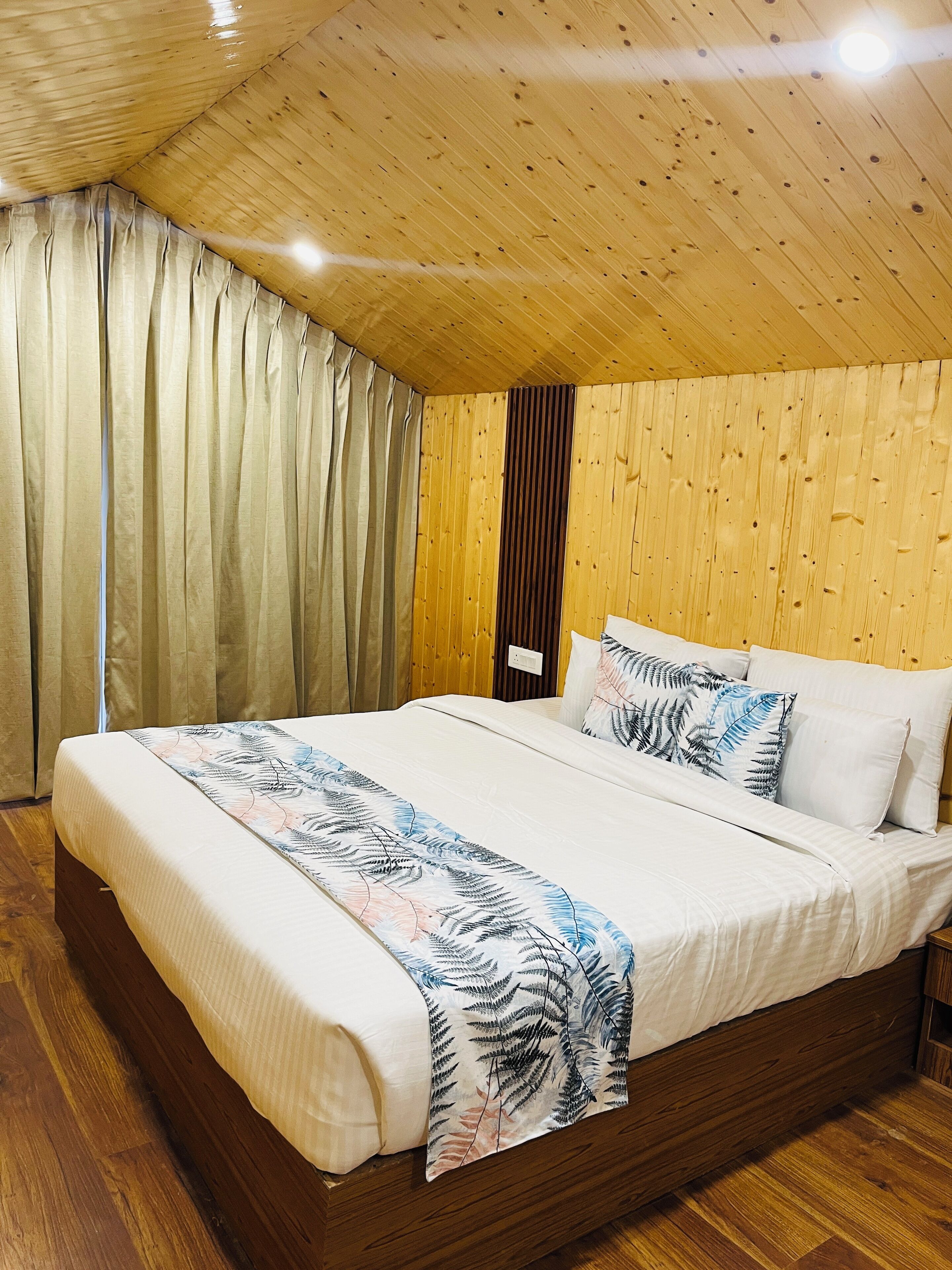 A bedroom with a wooden ceiling, a bed with white bedding, and a curtain on the window.
