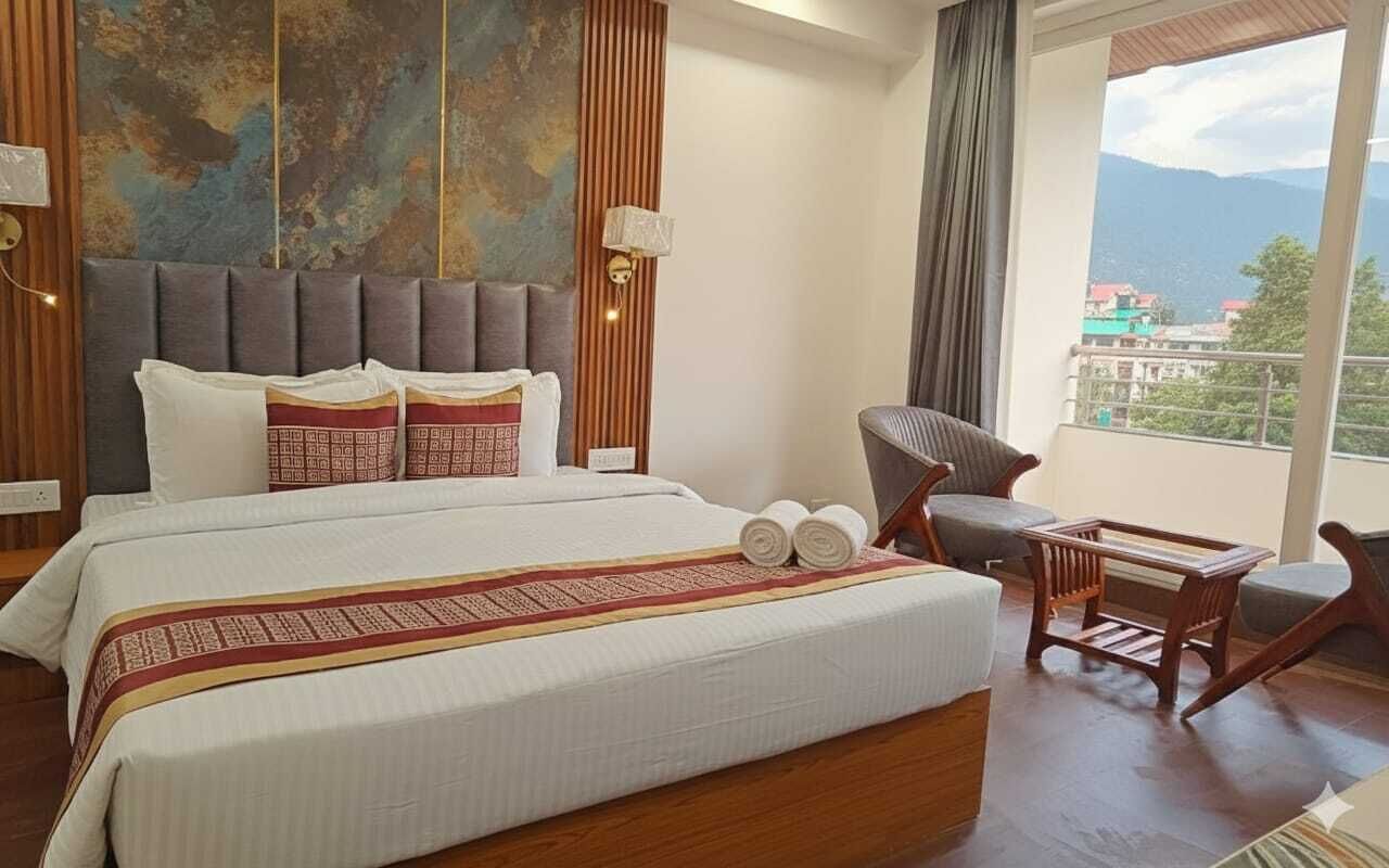 Habitación de hotel con una cama grande, cabecero de madera, vistas a montañas y un balcón con una silla.
