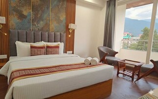 Habitación de hotel con una cama grande, cabecero de madera, vistas a montañas y un balcón con una silla.
