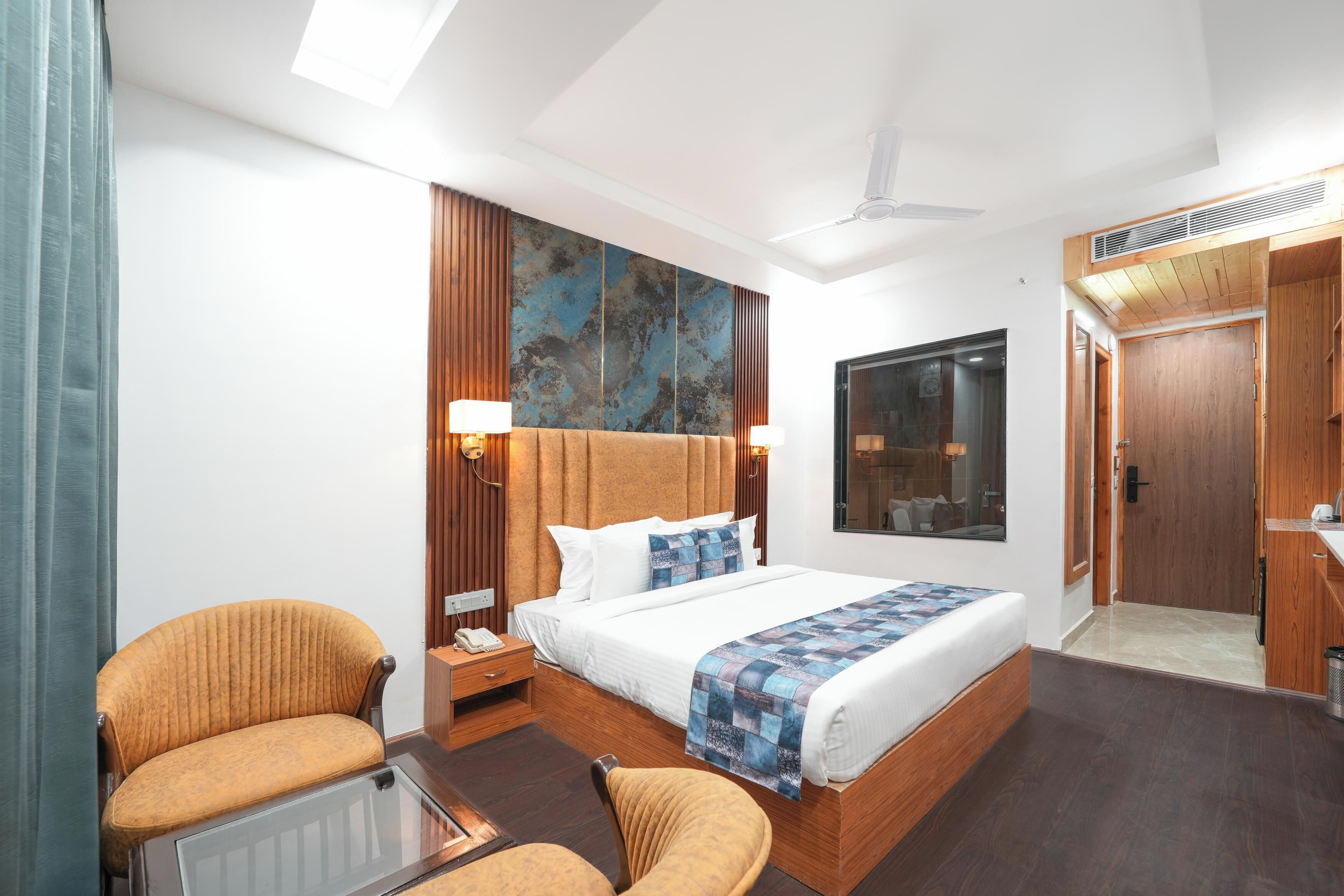 Une chambre d’hôtel moderne avec un grand lit, une tête de lit en bois, deux tables de chevet avec des lampes, une petite table avec une chaise et une grande fenêtre.