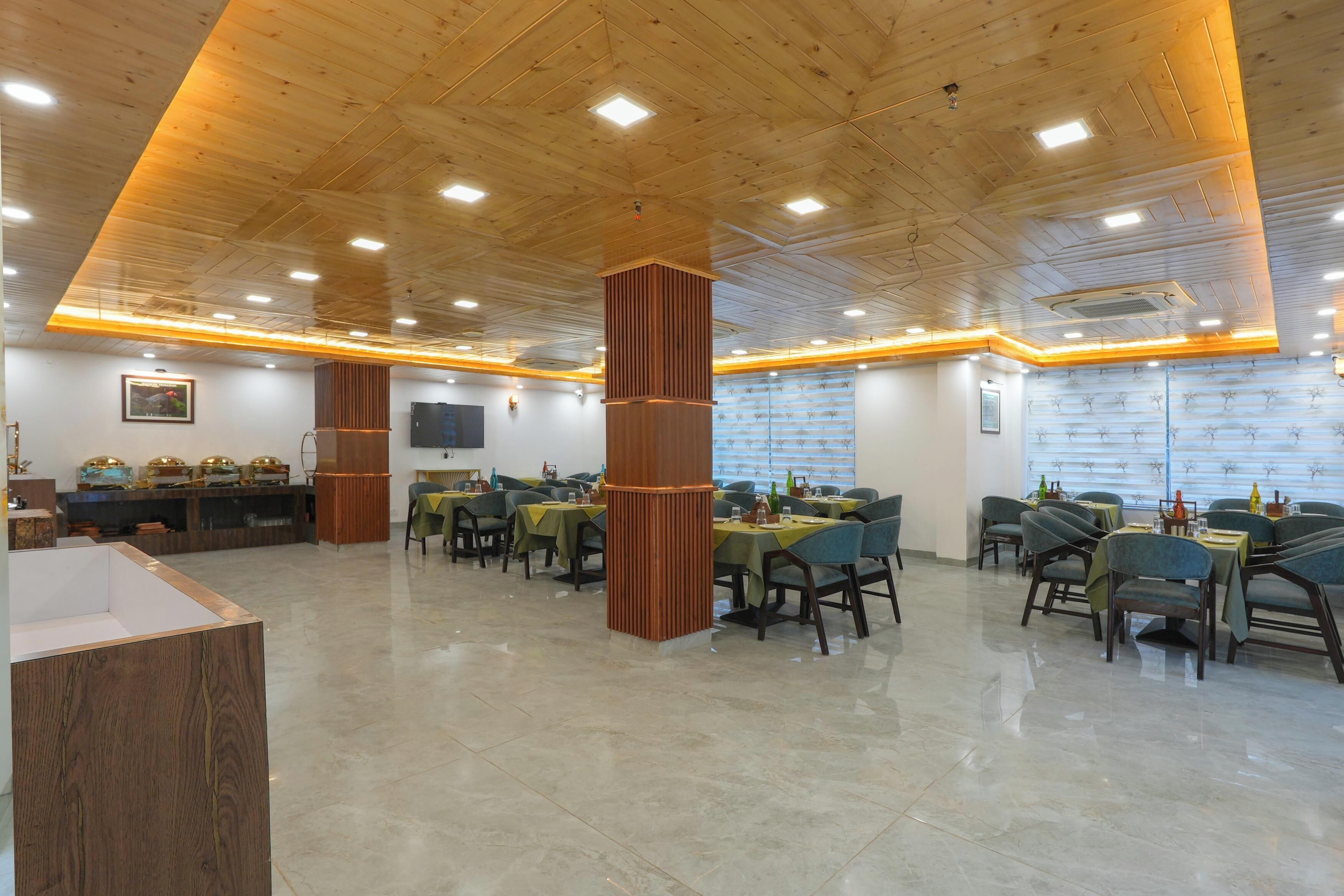 Un restaurante espacioso con paneles de techo de madera e iluminación empotrada. Las mesas están dispuestas con sillas, y hay objetos decorativos sobre ellas.