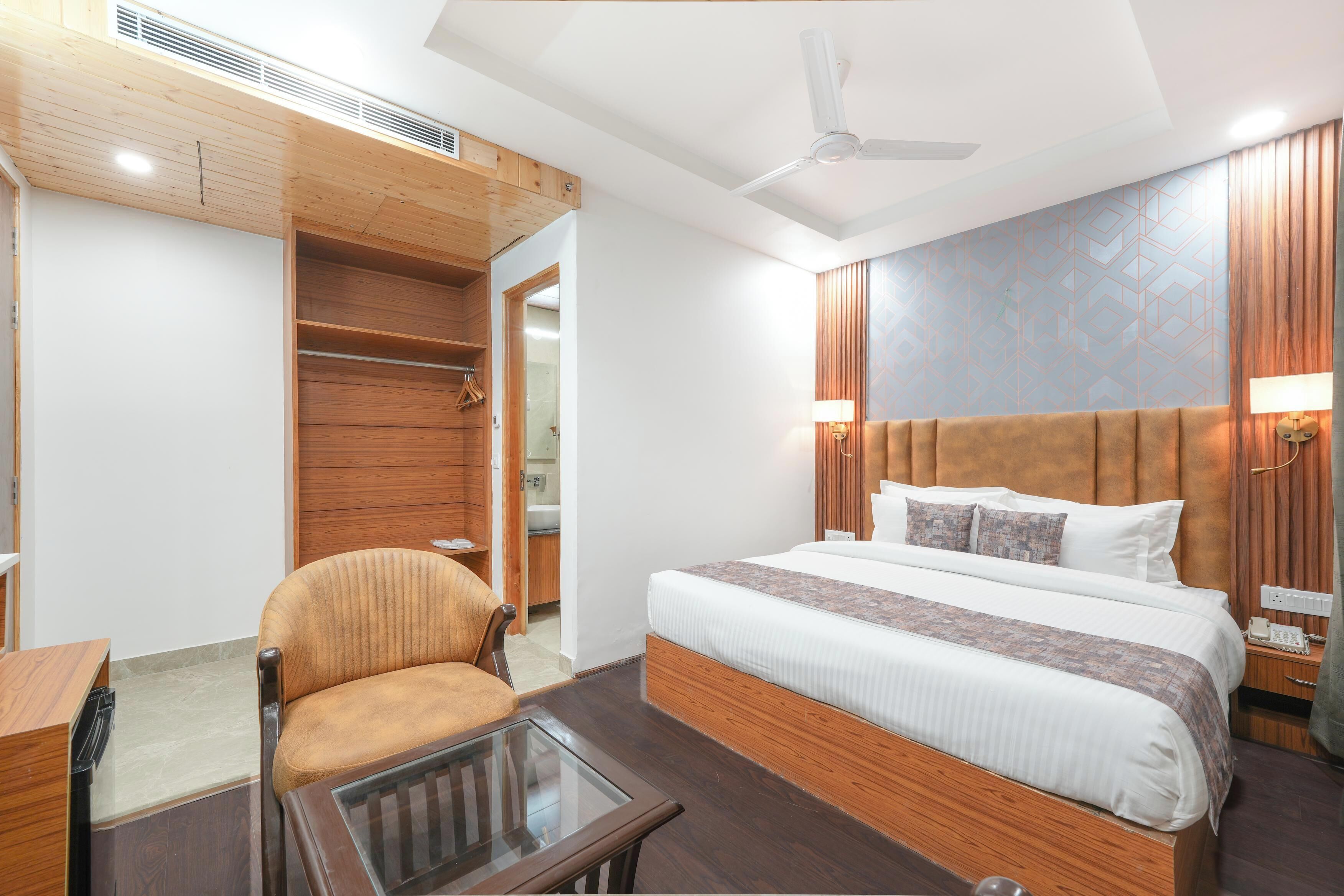 A hotel room with a bed, a wooden headboard, a glass table, a chair, and a wardrobe.