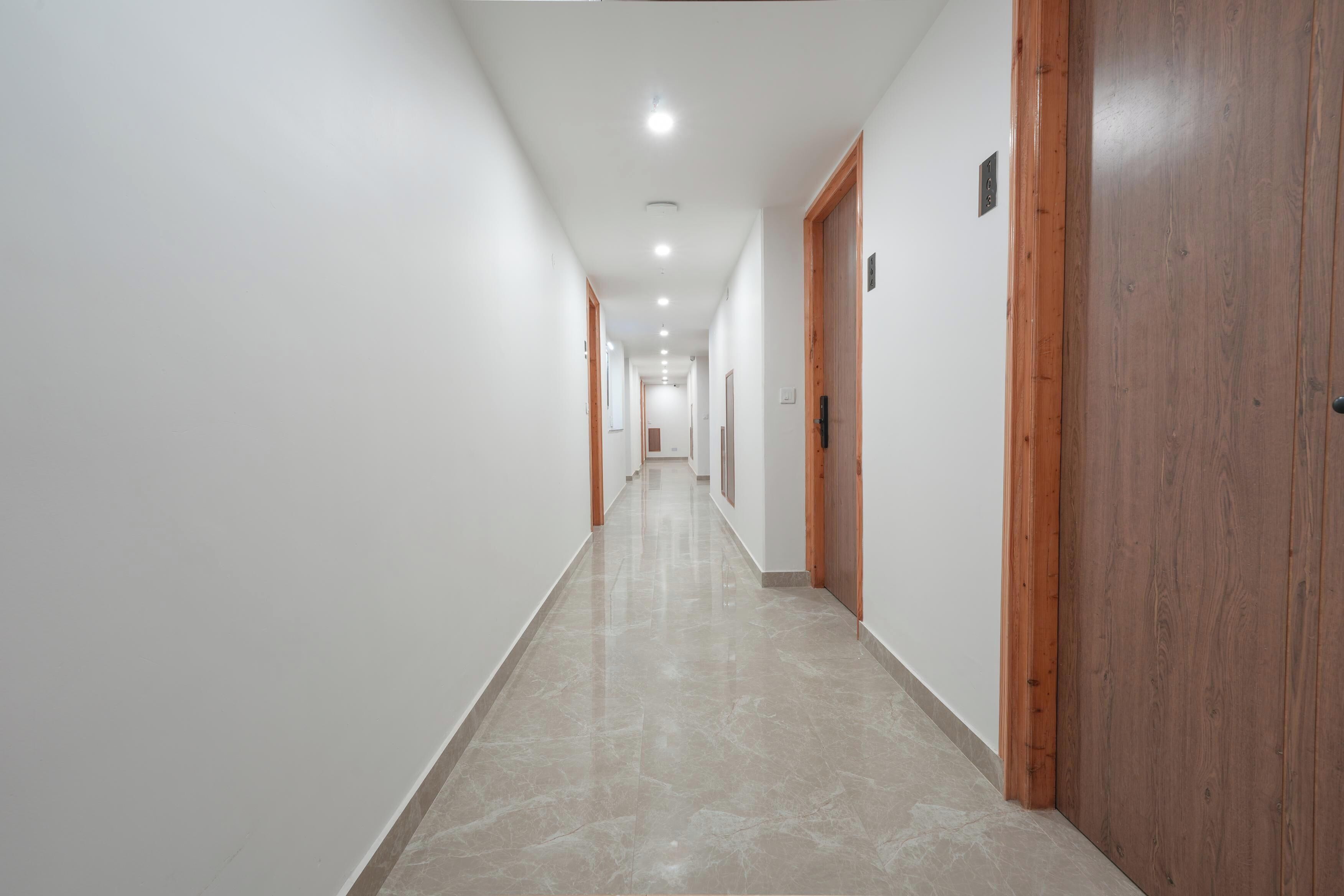 Un pasillo largo y estrecho con paredes blancas y suelo pulido, que da a varias puertas.
