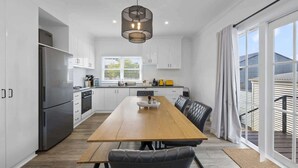 Een moderne keuken met witte kasten, een roestvrijstalen koelkast, een houten eettafel en een zwarte stoel.