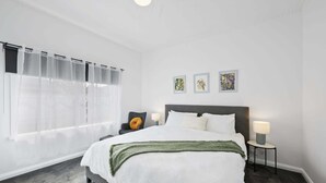 Een slaapkamer met een groot bed, een stoel met een geel kussen en drie ingelijste foto's aan de muur.