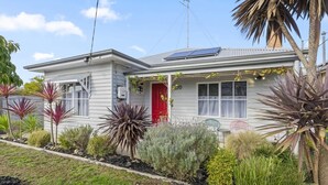 Een gelijkvloers huis met een rode deur, zonnepanelen op het dak en diverse planten in de voortuin.