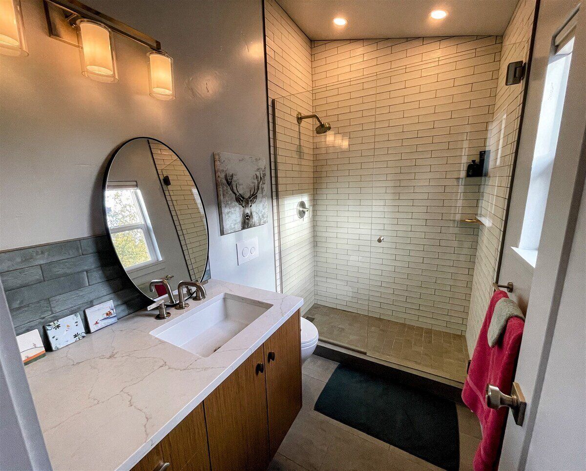 A bathroom with a white-tiled shower, a sink with a mirror, and a wooden vanity.