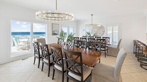 Un'ampia sala da pranzo con un grande tavolo in legno e sedie, due lampadari e ampie finestre con vista sull'oceano.