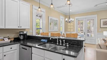 A kitchen with white cabinets, a black countertop, stainless steel sink, and pendant lighting.