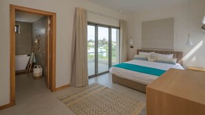 A modern bedroom with a large bed, a wooden desk, and a view of the outdoors through a sliding glass door.