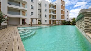 A modern apartment building with a swimming pool, wooden deck, and balconies.