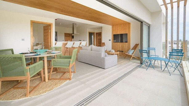 A modern living room with a dining area, a sofa, and a TV mounted on the wall.