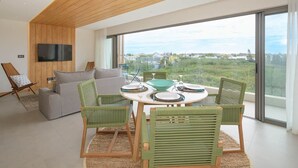 A modern living room with a wooden ceiling, a large window with a city view, a round dining table with chairs, and a TV mounted on the wall.