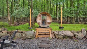 A rustic wooden structure in a forest setting, surrounded by rocks and a gravel path.