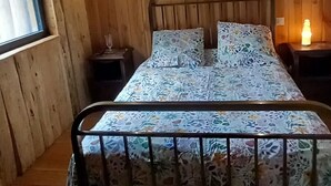 A wooden cabin bedroom with a bed, two bedside tables, and a window. - Wooden house in the fields (orcival)