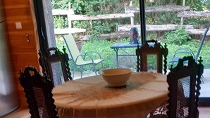 A dining table with a tablecloth, surrounded by four chairs, in a room with wooden flooring and a large window. - Wooden house in the fields (orcival)