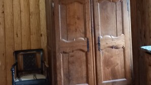 A wooden-paneled room with a large wooden wardrobe, a chair, and a bed with a floral bedspread. - Wooden house in the fields (orcival)
