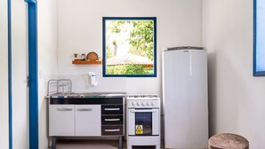 Eine kompakte Küchenzeile mit Herd, Backofen und Spüle. Ein kleines Regal beherbergt Küchenutensilien, und ein gerahmtes Foto eines Gartens ist an der Wand angebracht.