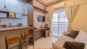 Ein modernes Wohnzimmer mit einer Couch, einem Fernseher und einem Balkon mit Vorhängen.