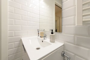 Un baño con azulejos blancos tipo metro, un lavamanos blanco, un espejo y un dispensador de jabón.