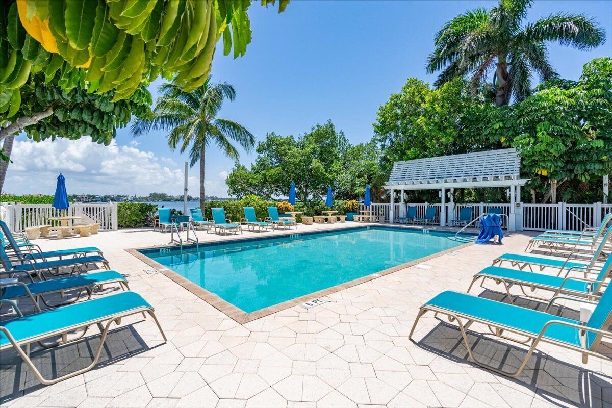 Un espace piscine avec des chaises longues bleues, une piscine et un coin salon abrité.