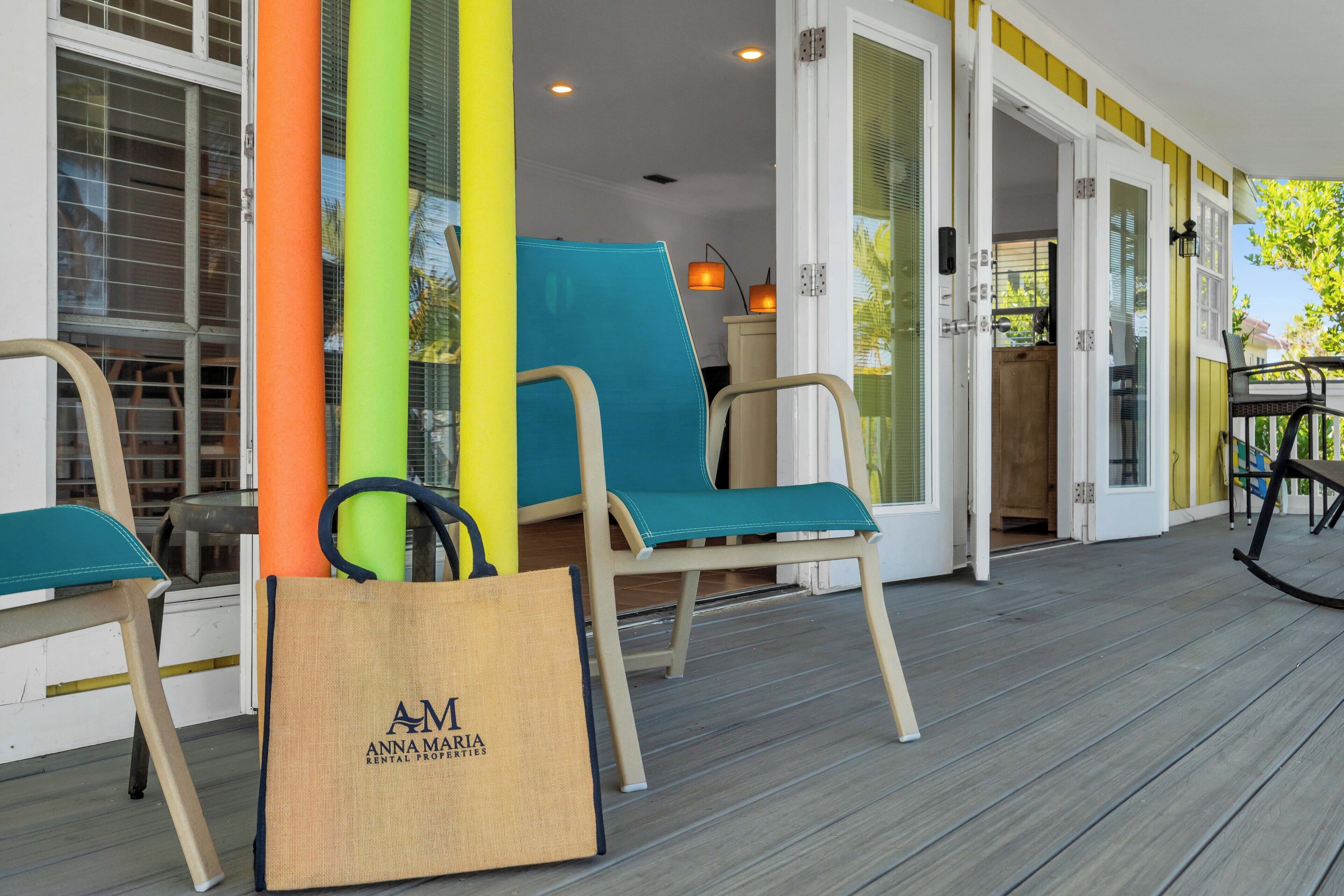 A wooden deck with two chairs, a surfboard, and a rental property bag.