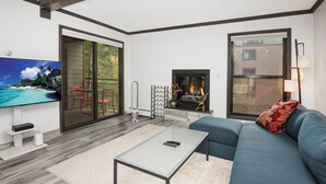 A modern living room with a sofa, a coffee table, a TV, a fireplace, and a sliding glass door leading to a balcony. - Modern Vail Condo, steps to Free Shuttle | BW222 (Vail)