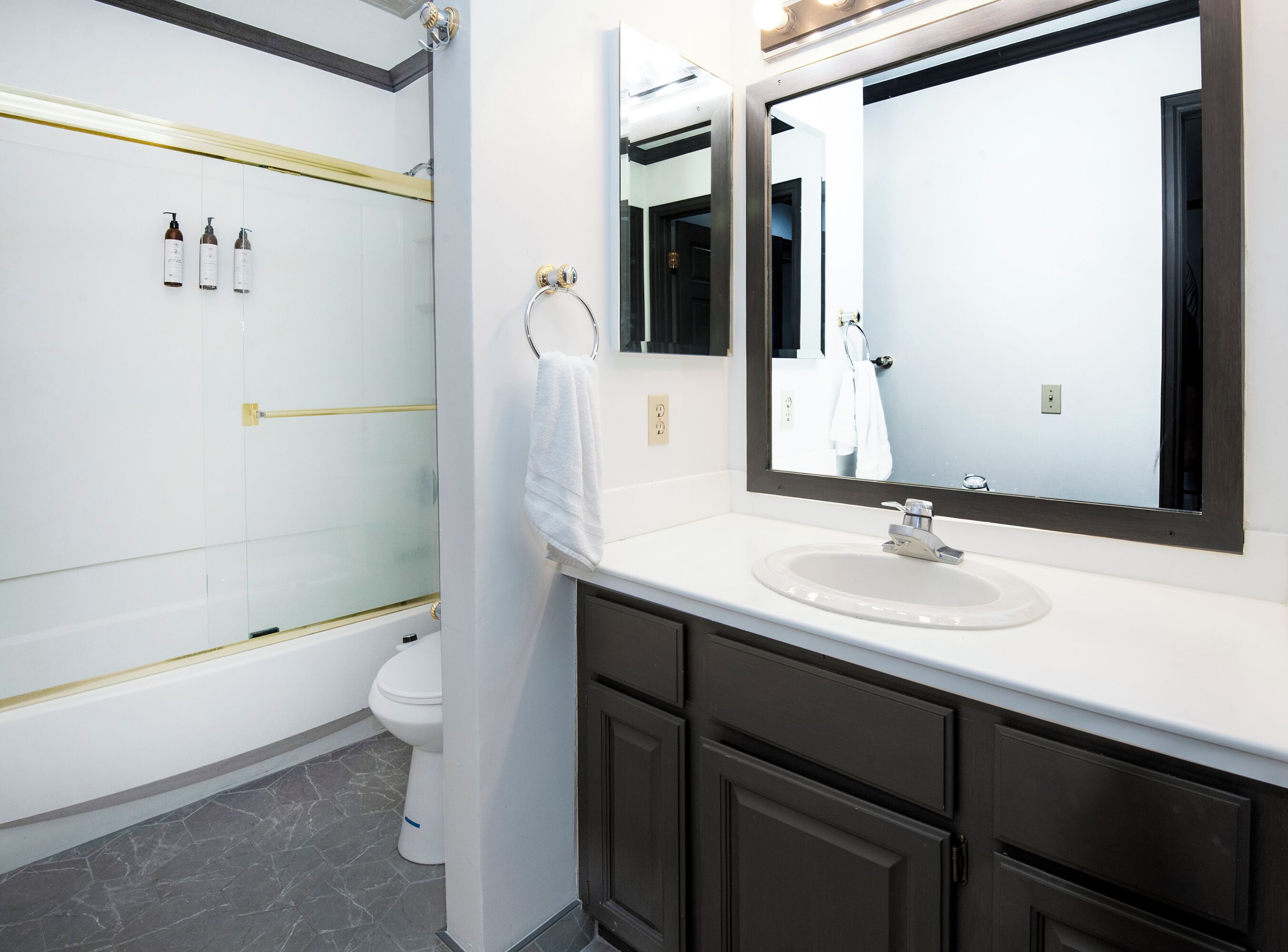 Une salle de bain moderne avec une douche à parois de verre, un lavabo blanc, des meubles sombres et un grand miroir.