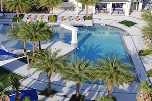 A swimming pool with palm trees, lounge chairs, and a building with a white facade.