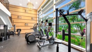 Ett gym med träningsutrustning, stora fönster och utsikt över grönområden.
