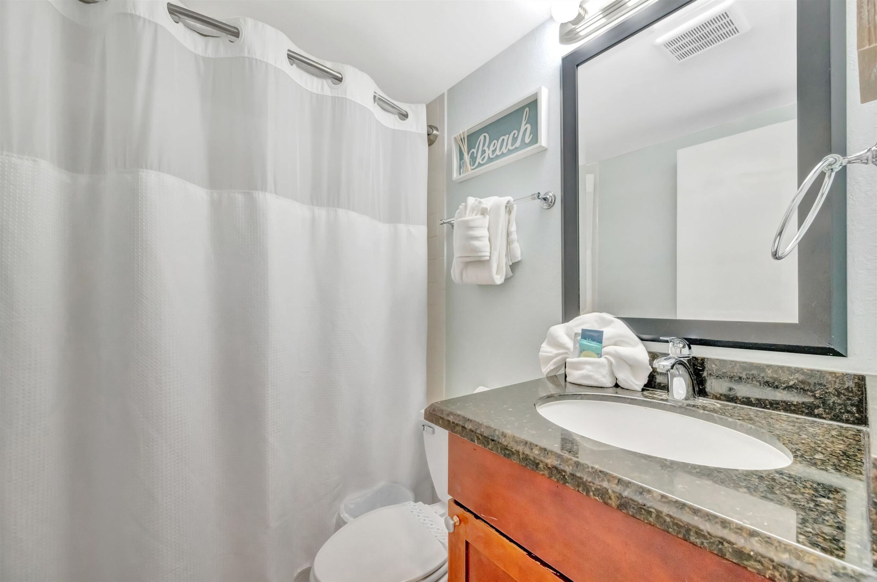 A bathroom with a shower curtain, a sink with a mirror, and a towel rack.