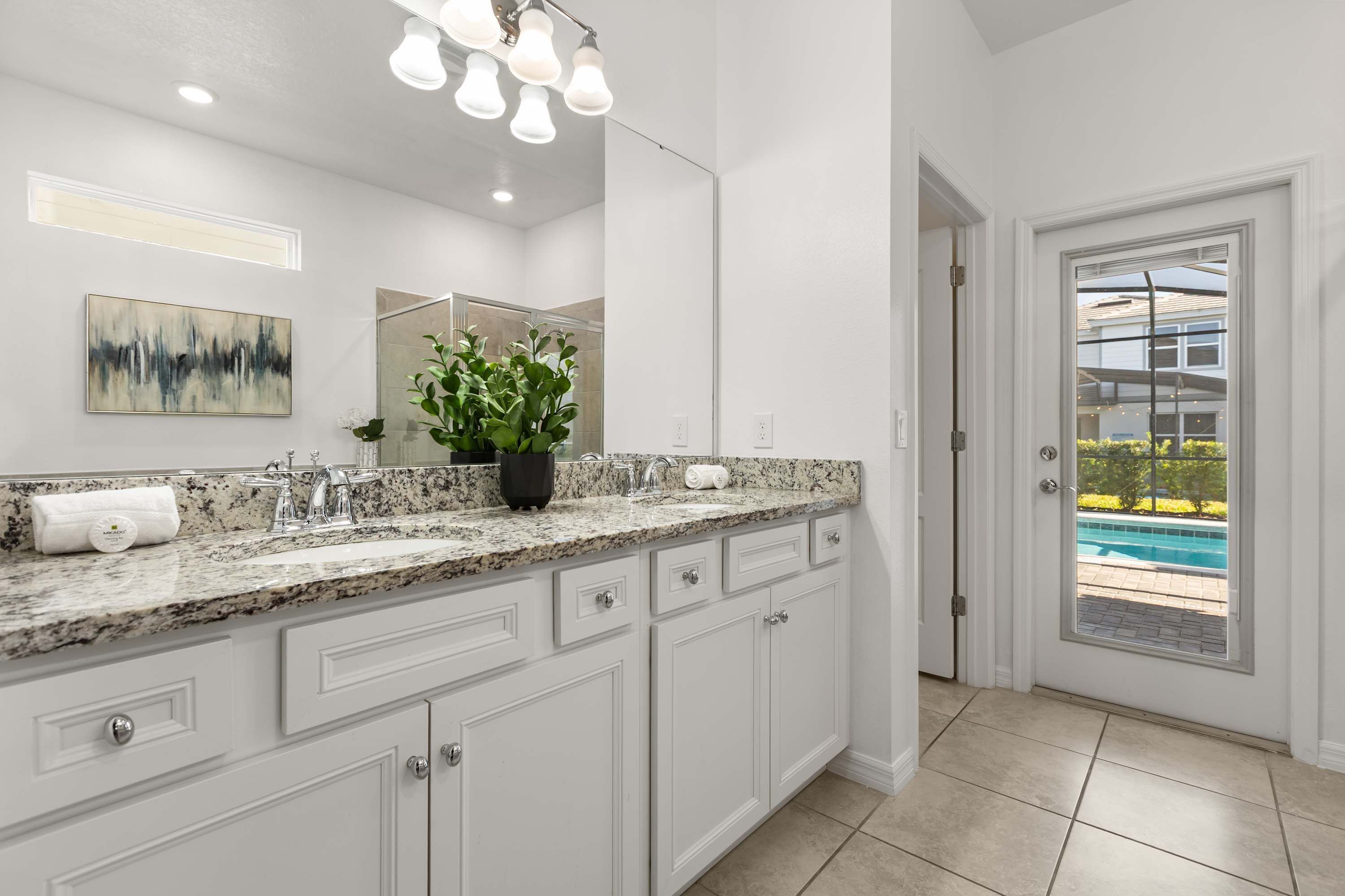 A modern bathroom with a granite countertop, white cabinetry, a large mirror, and a potted plant.