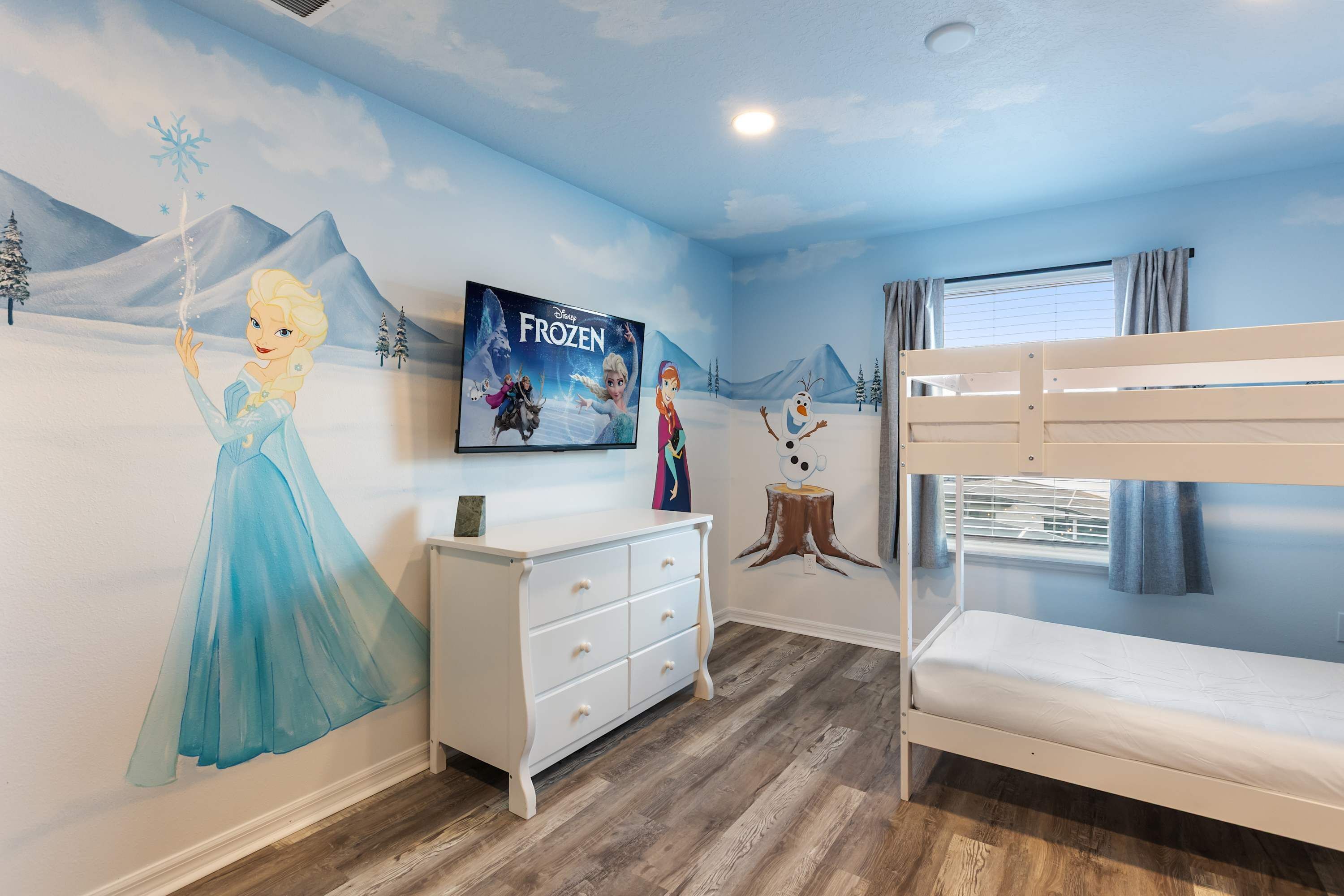 A child's bedroom with a mural of Frozen characters, a bunk bed, a dresser, and a window with curtains.