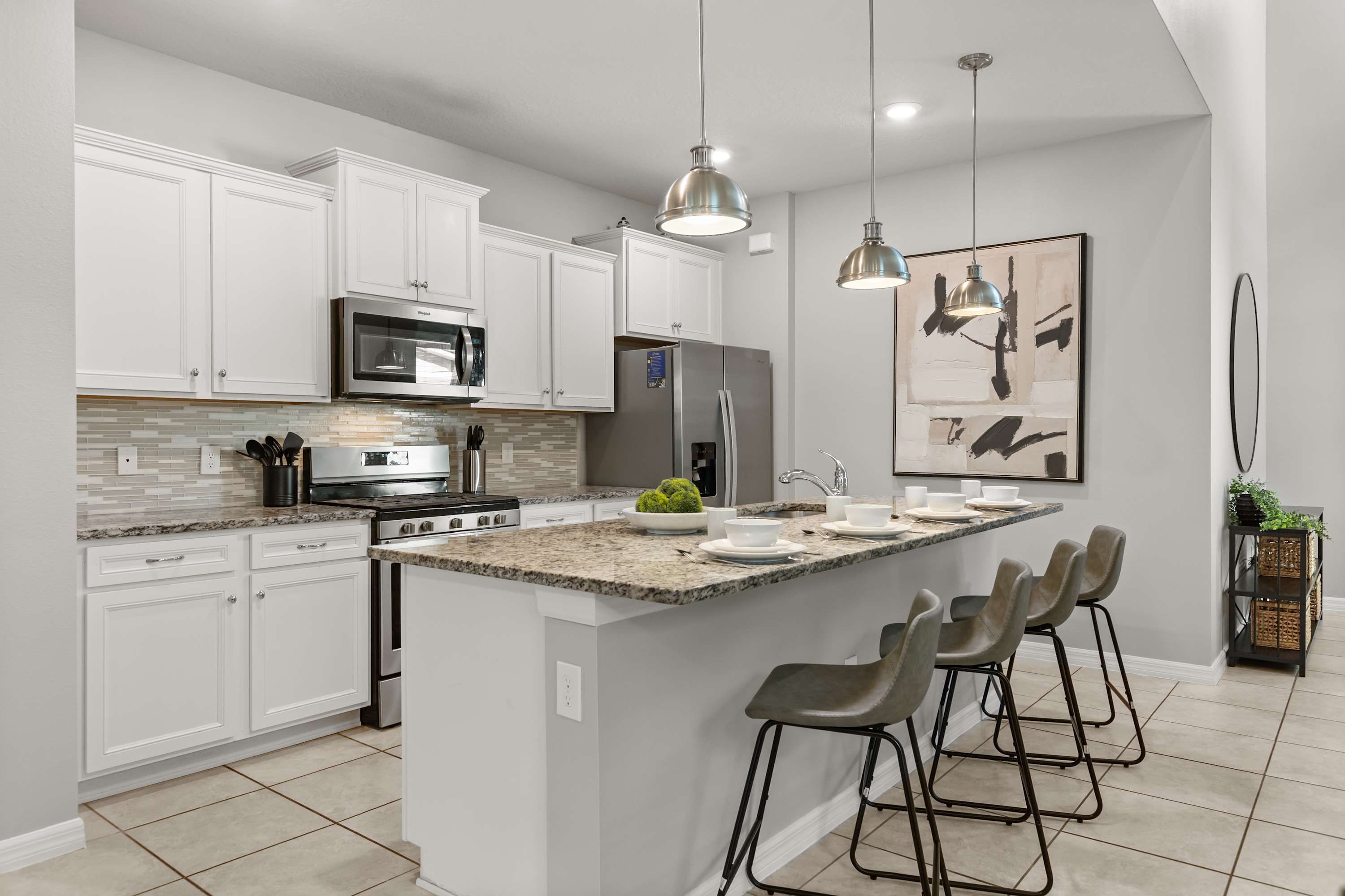 Una cocina moderna con armarios blancos, una isla central con taburetes, electrodomésticos de acero inoxidable e iluminación colgante.