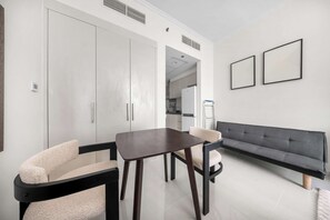 Una sala de estar moderna con un sofá, una mesa de comedor con sillas, y un área de cocina visible a través de un vano abierto.